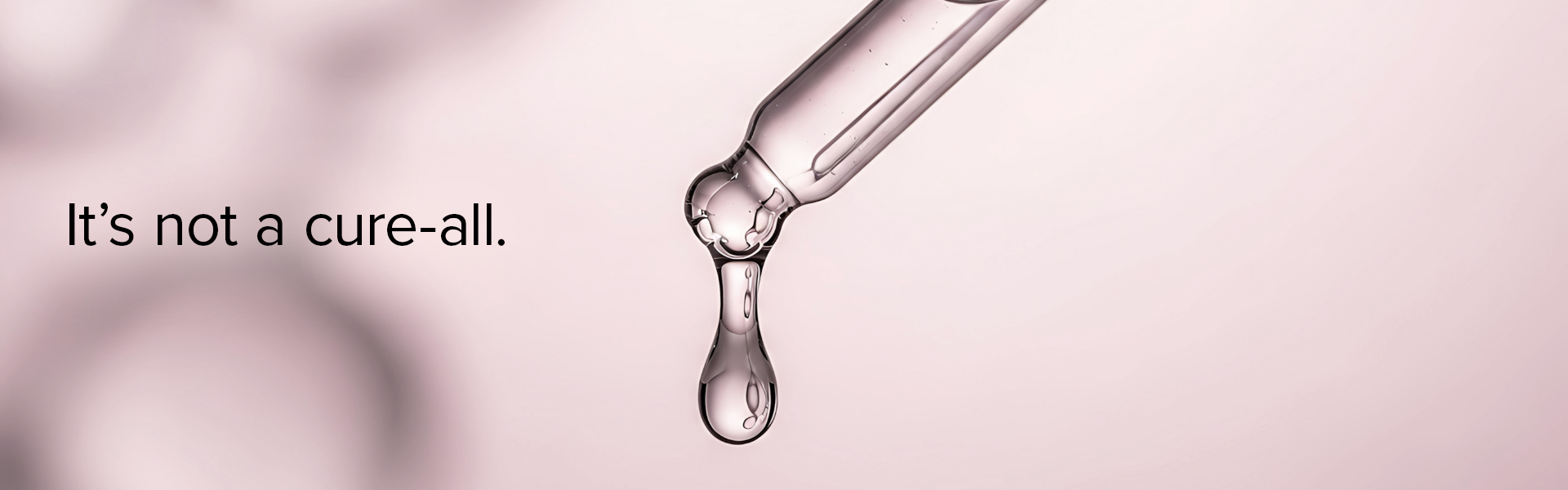 Close-up of a liquid drop falling from a glass dropper against a soft pink background