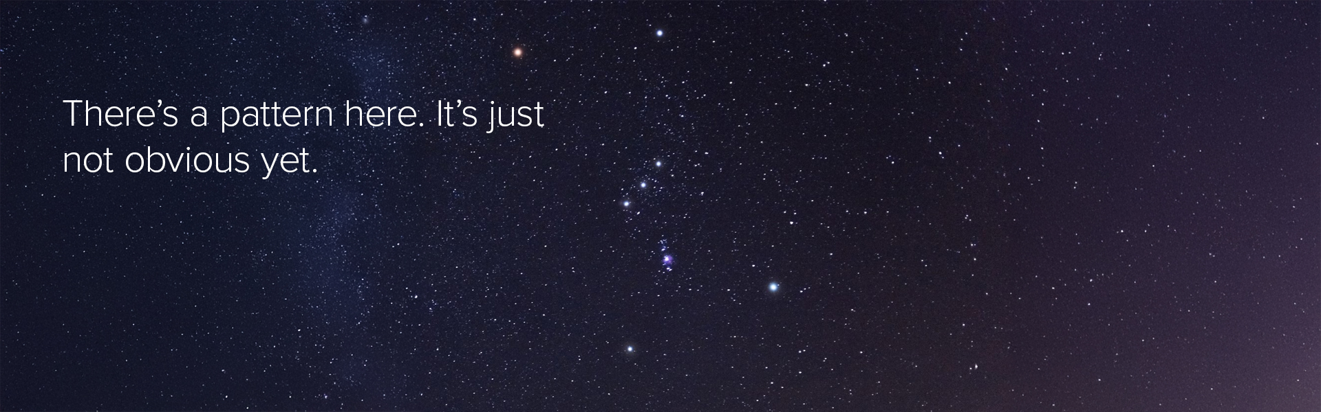 A night sky filled with stars, with a small cluster of brighter stars near the center forming a subtle shape